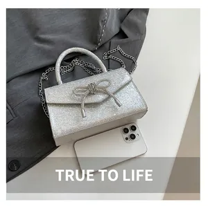 Close-up of glitter silver bow handbag with chain strap showing size scale with a phone