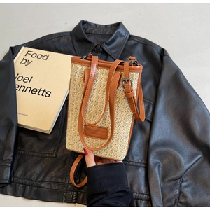 Détail d'un sac seau en paille avec bordure en cuir marron sur une veste en cuir noir