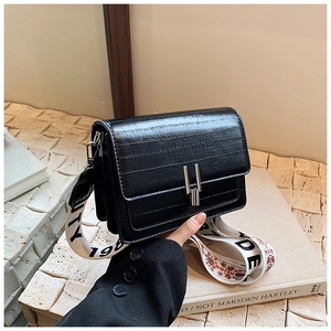 Close-up of black glossy oil wax leather bag with metallic buckle and floral strap