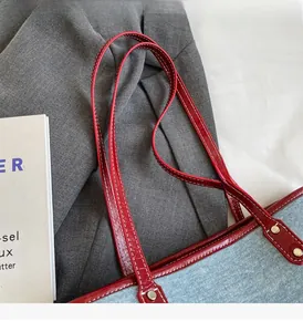 Close-up of red leather handle with white stitching on light blue denim tote bag