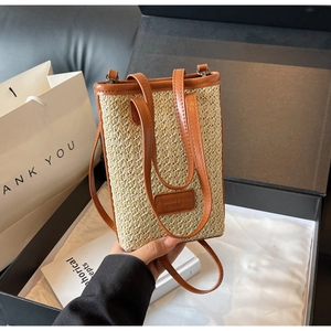 Detail of a straw woven crossbody bag featuring brown leather trim and stylish dual straps
