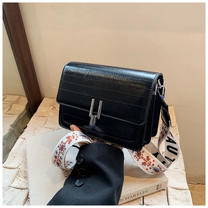 Detail of black textured square crossbody bag with silver hardware and embroidered strap