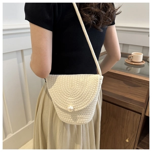Piccola borsa a tracolla in paglia beige con perla, indossata da una modella in casa