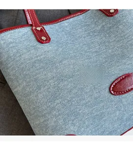 Detail of light blue denim tote with red leather piping and white contrast stitching