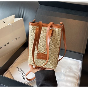 Straw mini crossbody bag with brown leather trim inside an elegant black gift box