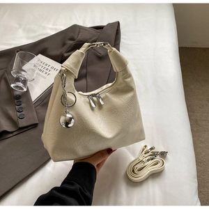Close-up of cream pleated handbag with silver dual zippers and metallic ball charm detail
