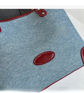 Close-up of denim texture with red faux crocodile trim and silver rivets on tote bag