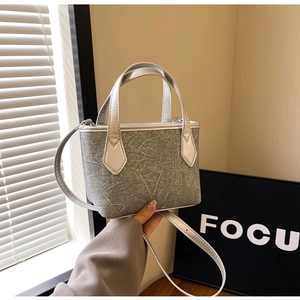 Détail du sac seau en denim gris avec anses en cuir argenté et texture marbrée chic