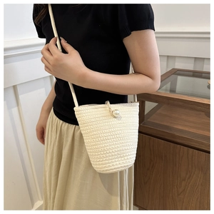 Dettaglio di una borsa a secchiello in paglia bianco crema con decorazione in maxi perla