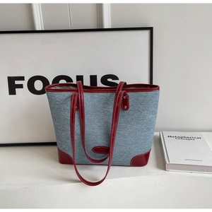 Detail of denim tote bag with red leather trim, contrast stitching and metal rivets