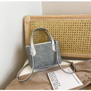Détail du sac seau minimaliste avec texture marbre et anses argentées posé sur une chaise