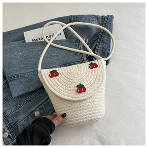 Dettaglio di una mini borsa di paglia bianca intrecciata con tre ciliegie ricamate rosse