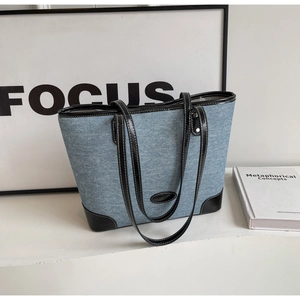 Detail of blue denim tote bag with black leather trim and white contrast stitching