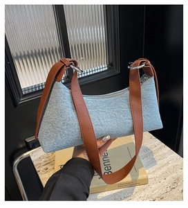 Close-up of blue denim baguette bag with brown leather strap and silver ring hardware