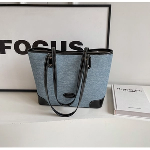 Close-up of denim tote bag with black leather edges and silver rivet reinforcement