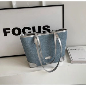 Detail of blue denim tote bag with silver leather trim and oval metal plaque