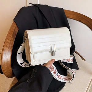 Chic cream-colored leather crossbody bag with embroidered wide strap on a blazer