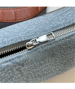 Close-up of smooth metal zipper and brown litchi leather strap on denim shoulder bag