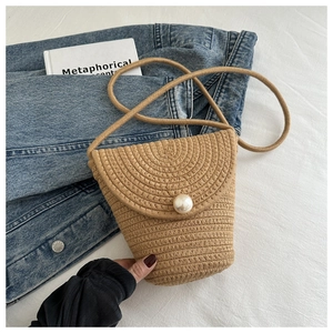Dettaglio borsa in paglia intrecciata kaki con perla sintetica su giacca di jeans