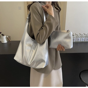 Close-up of a large silver metallic hobo bag and matching zippered pouch on a modern desk