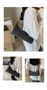 Detail view of grey denim underarm bag with brown leather strap and silver metal buckle