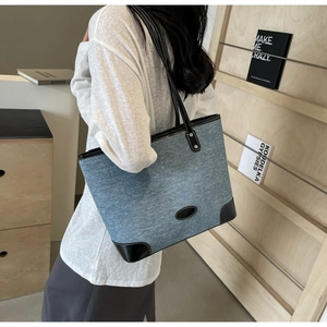 Detail of denim tote bag with black leather handles and reinforced base corners