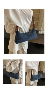 Detail of dark blue denim underarm bag with adjustable brown leather strap and silver buckle