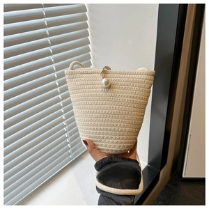 Dettaglio della borsa a secchiello beige intrecciata a mano con perla e tracolla in corda