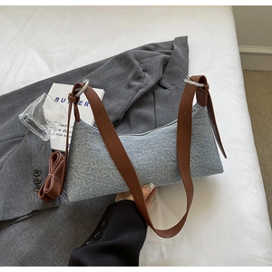 Close-up of blue-grey denim underarm bag with brown leather strap and silver ring detail