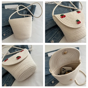 Dettaglio borsa a secchiello intrecciata crema con ricamo di ciliegie e tracolla in cotone