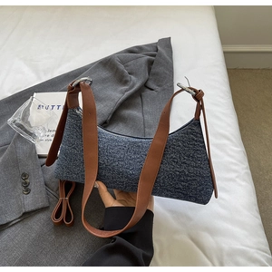Detail of denim shoulder bag featuring brown leather strap and silver metal rings