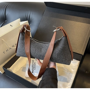 Detail showing grey tweed baguette bag with brown leather strap in a premium gift setup