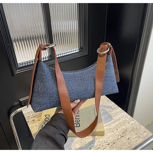 Detail of denim shoulder bag with brown leather trim and silver metal buckle hardware