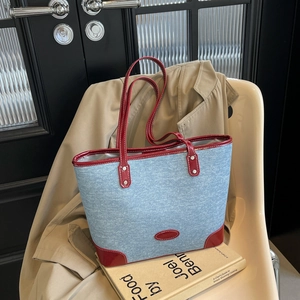 Blue denim tote bag with red glossy trim and silver rivets shown in a stylish room