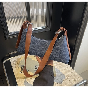 Detail of dark blue denim underarm bag with brown leather strap and silver metal rings
