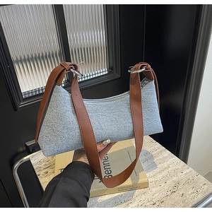 Detail of blue denim baguette bag featuring brown leather straps and silver metal hardware