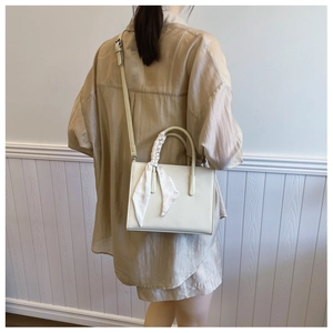 Schicke cremefarbene Leder-Tote mit elegantem Seidentuch-Griff an der Schulter eines Models