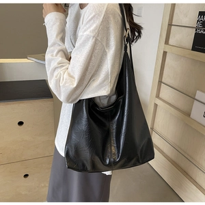 Detail of minimalist black tote bag featuring unique crinkled leather texture and gold metal buckle