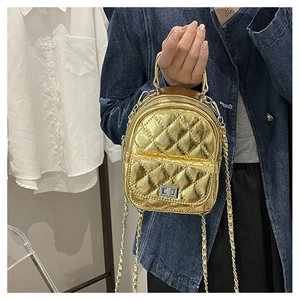 Close-up of golden quilted mini backpack with metal chain strap on denim outfit