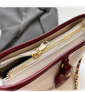 Close-up of smooth gold-tone zipper and wine red trim on a beige leather bucket bag