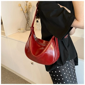 Detail einer dunkelroten Hobo-Tasche aus glänzendem Leder, getragen von einem Model
