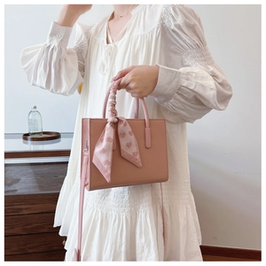 Detail der hellrosa Handtasche aus Narbenleder mit herzbedrucktem Schal am Griff
