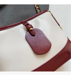 Detail of contrast color leather bucket bag showing beige and burgundy stitching and gold chain