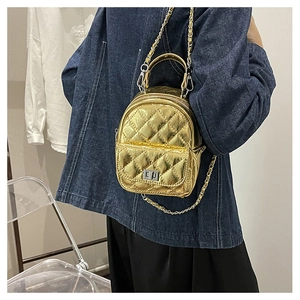 Detail of a shiny gold quilted mini backpack featuring a chain strap and metal twist lock