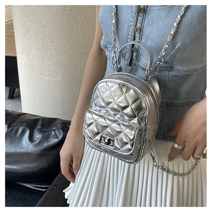 Detail of silver quilted mini backpack with metallic finish and chain strap on model