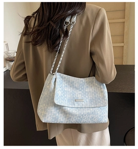 Detail of light blue tweed shoulder bag with silver chain worn by woman in brown blazer