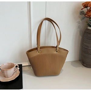 Detail of light brown pleated tote bag with golden metal rings and slim handles