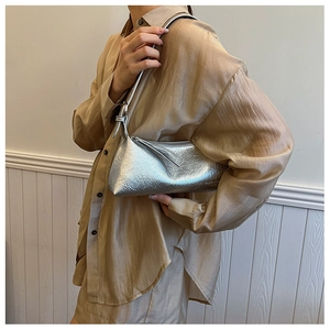 Silver metallic shoulder bag with crinkled texture worn over a beige pleated shirt