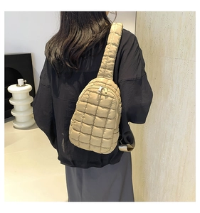 Rear view of a beige quilted nylon crossbody bag with wide padded shoulder strap on a model