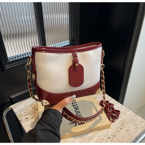 Detail of burgundy leather contrast bucket bag with gold chain strap and metal corner